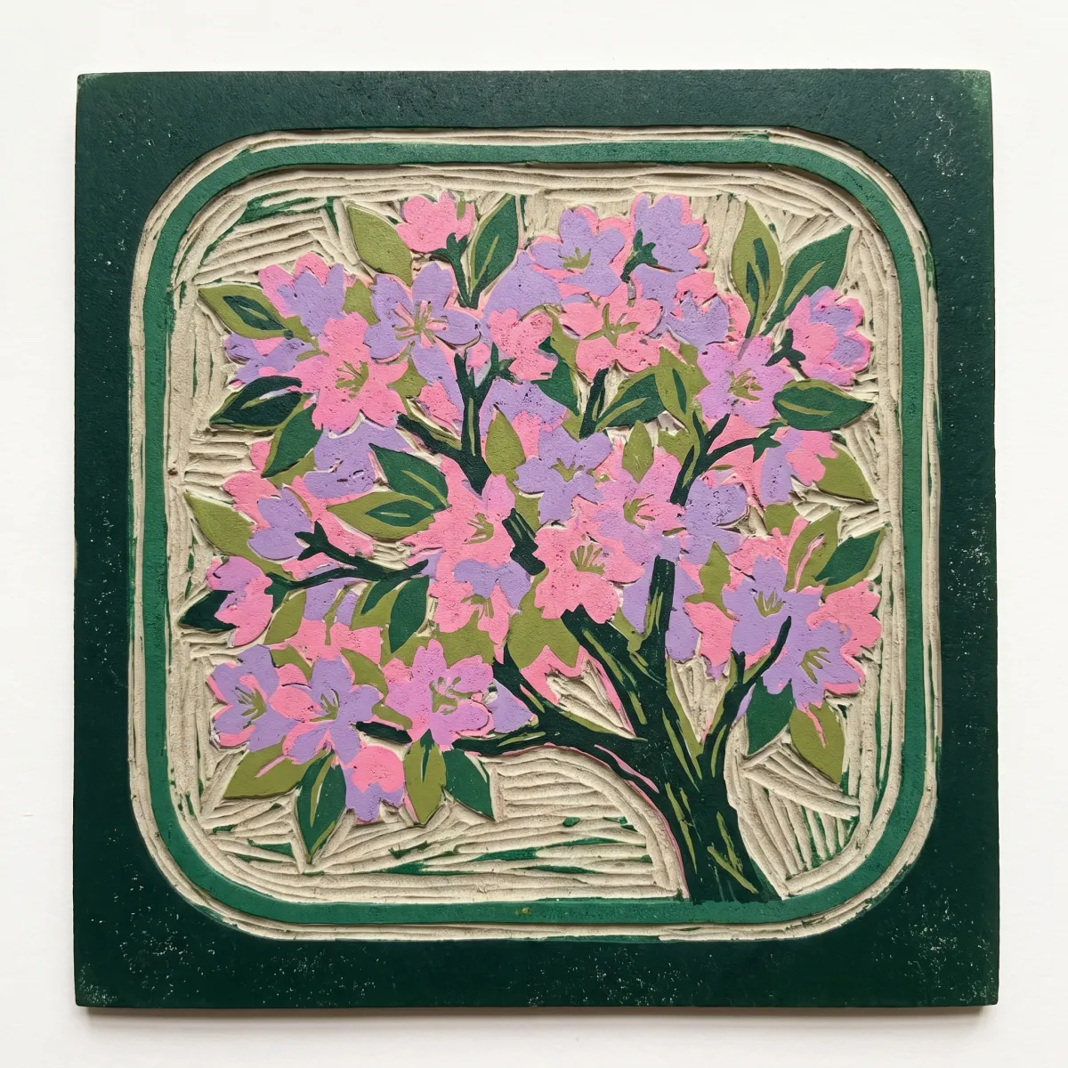 A linocut printing block carved with a cherry tree in bloom inside a window frame